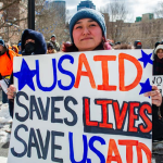 A woman holds a sign supporting USAID as demonstrators rally against US President Donald Trump and his policies during a protest near the Massachusetts Statehouse on Presidents' Day on February 17, 2025, in Boston, Massachusetts. (Photo by Joseph Prezioso / AFP