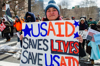 A woman holds a sign supporting USAID as demonstrators rally against US President Donald Trump and his policies during a protest near the Massachusetts Statehouse on Presidents' Day on February 17, 2025, in Boston, Massachusetts. (Photo by Joseph Prezioso / AFP